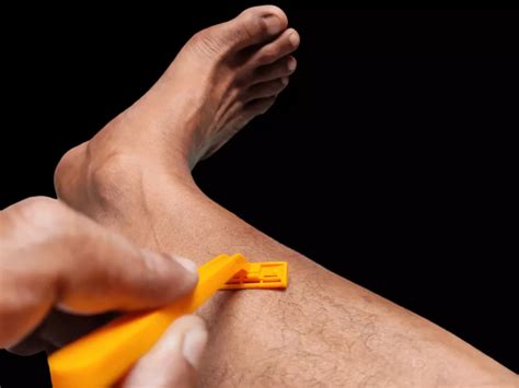 Muž si holí nohy žiletkou